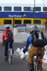 two people on bikes, riding towards a North Star Rail car