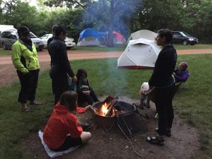 Several grease rag travelers gathered around a campfire, roasting marshmallows, tents in background