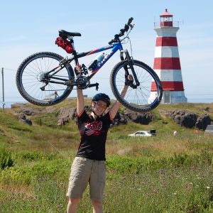 Author holding bike over head in field, lighthouse in the background.
