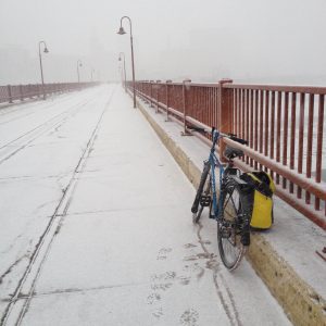 bike resting against a bridge in a very snowy and snowing setting