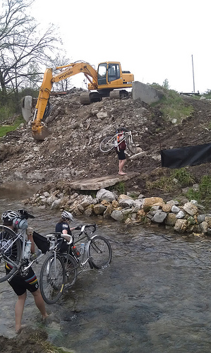 cyclists crossing a construction area with a backhoe