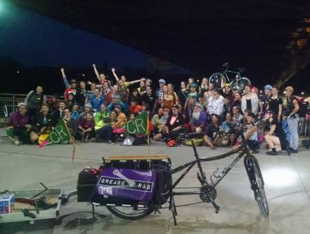 large group gathered for photo behind a bike in the foreground with a grease rag banner