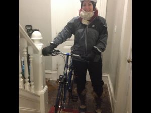 person dressed for a winter bike ride, with bike, in a house entry way